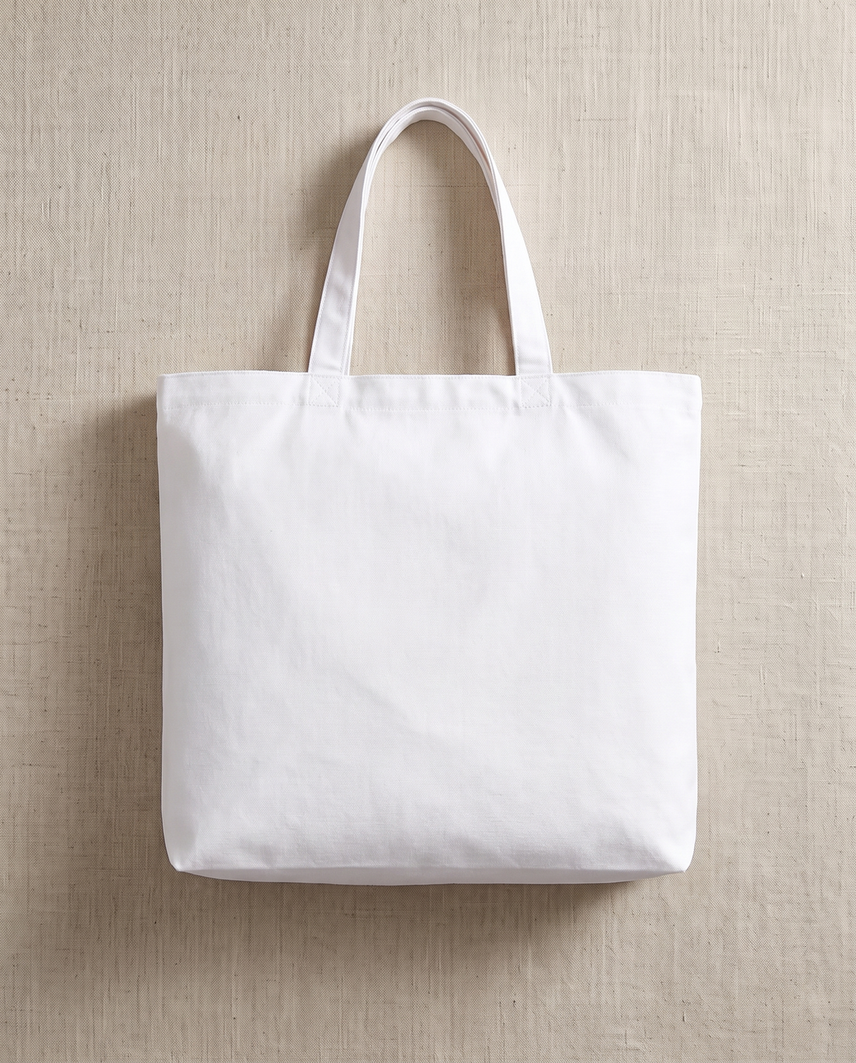 A blank white cotton canvas jumbo tote bag shot square-on, on warm off-white linen