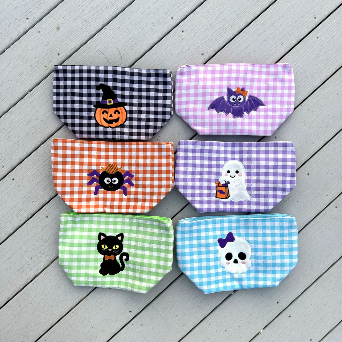 Six gingham baskets laid flat: pumpkin, bat, spider, ghost, black cat, and skull