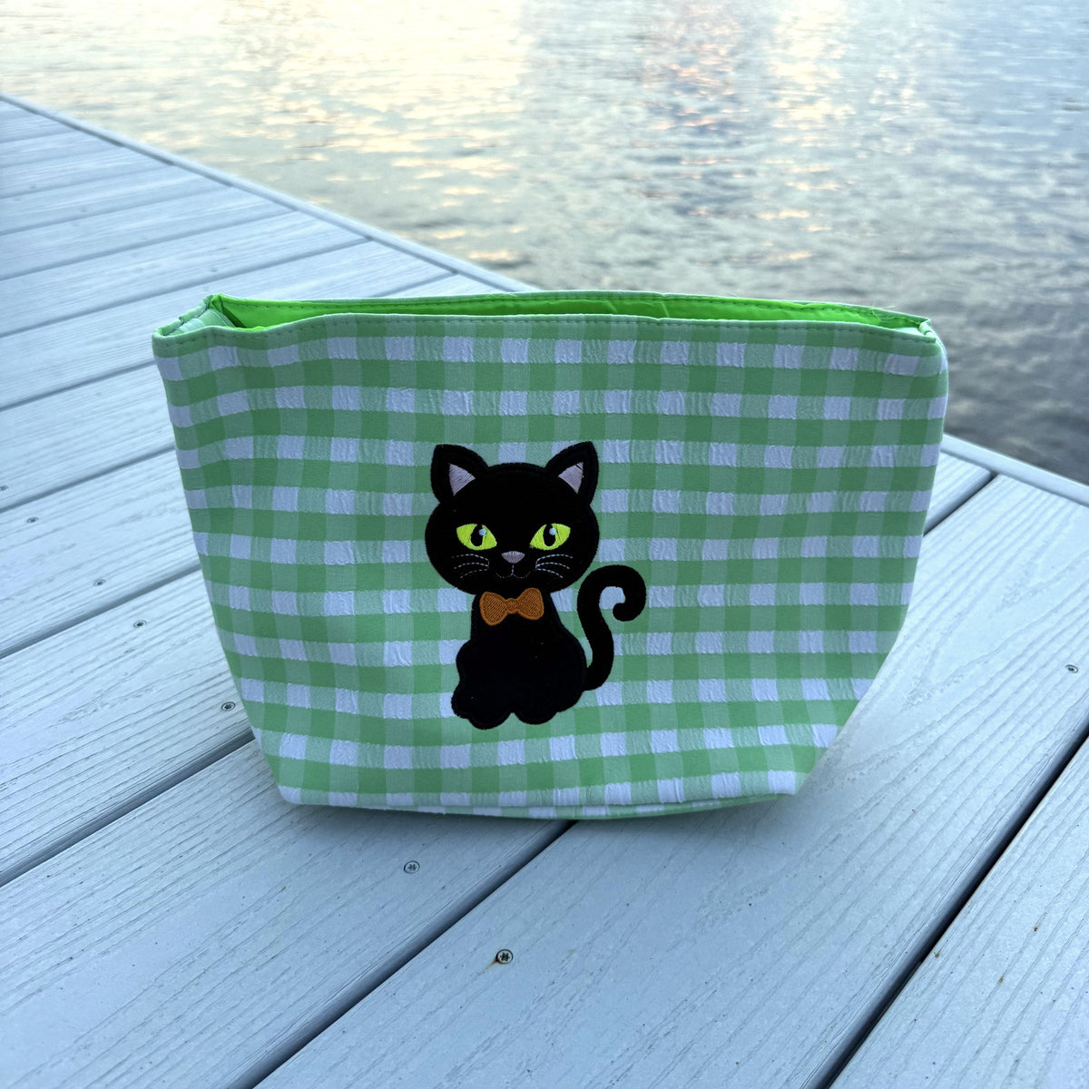Green gingham basket with a black cat wearing an orange bow