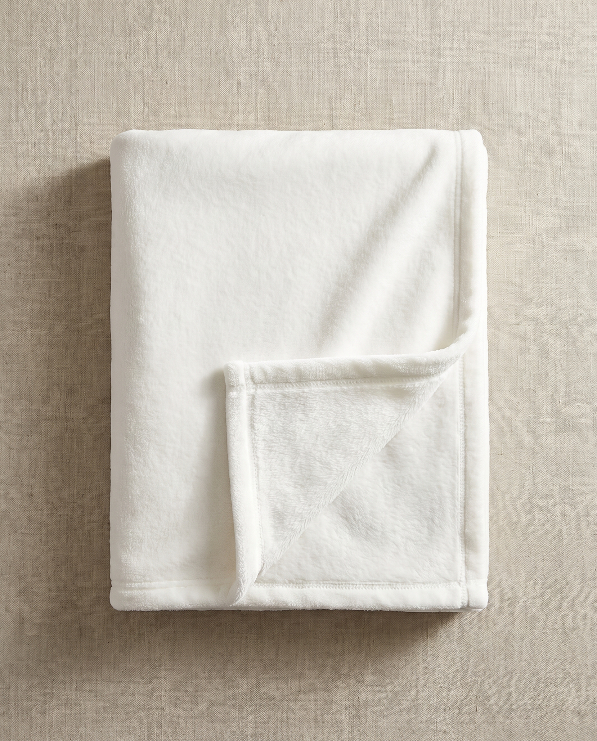 A blank white silk-touch baby blanket, folded and laid flat on warm off-white linen