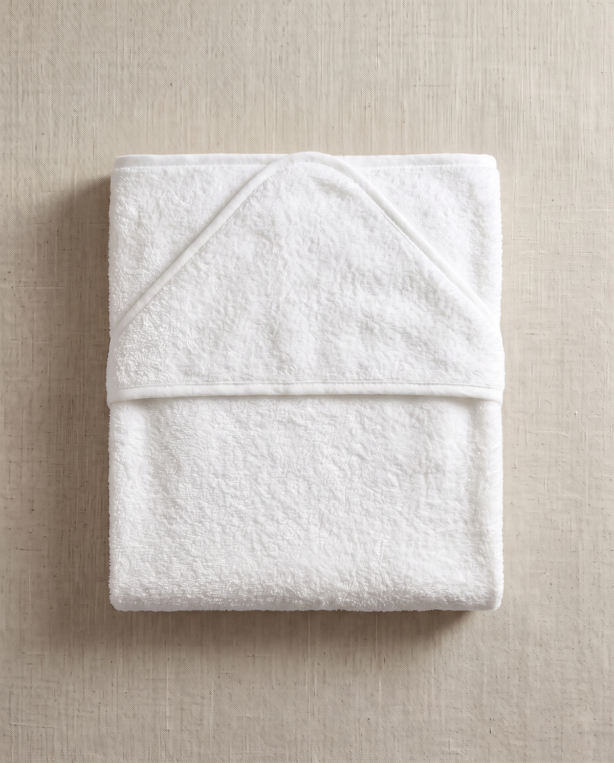 A blank white terry hooded baby towel on warm off-white linen